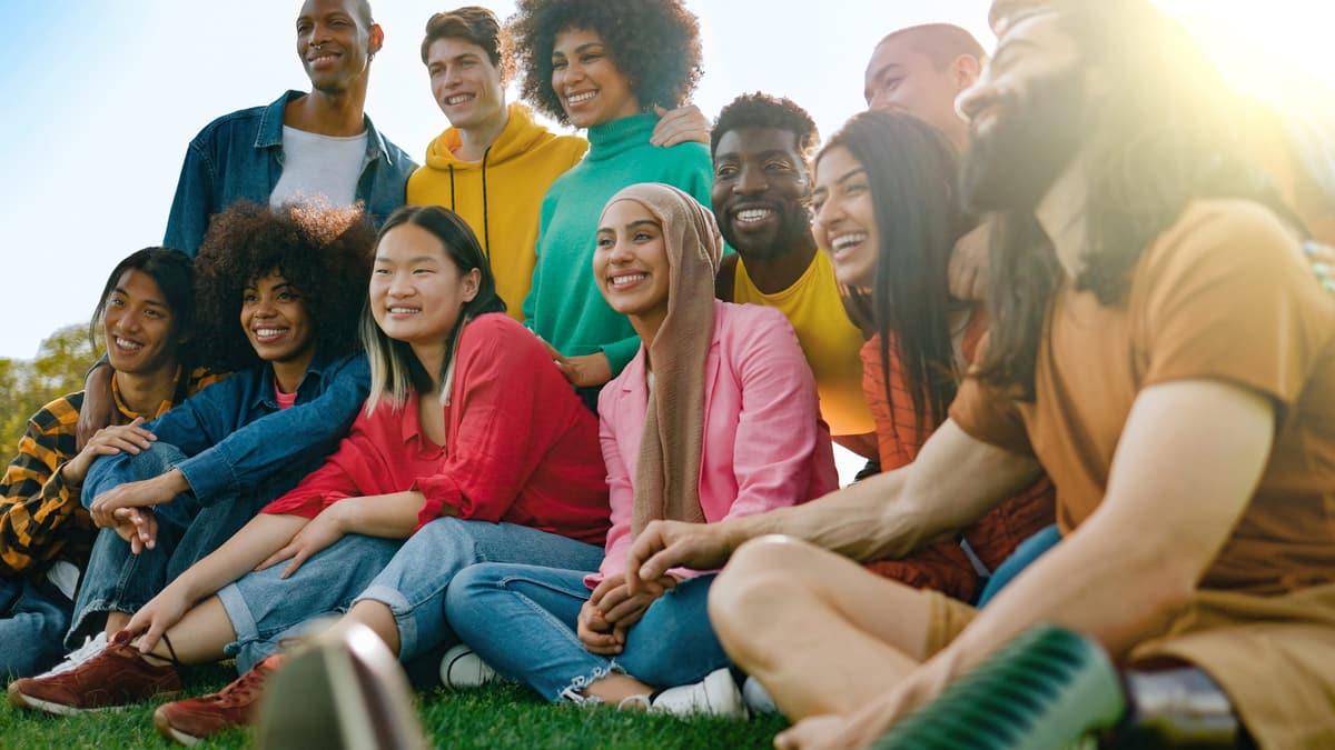 A group of young people from many backgrounds sitting together outdoors, smiling.